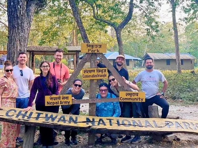 A group of tourists posing behind a Chitwan National Park wooden sign.