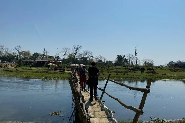Turistas caminando por una estrecha pasarela de madera sobre un río ancho