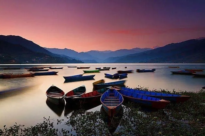 Plusieurs bateaux en bois reposant sur un lac calme lors d'un coucher de soleil éclatant.